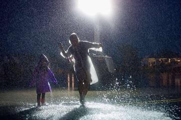 An adult and a child wearing raincoats and dancing in a puddle