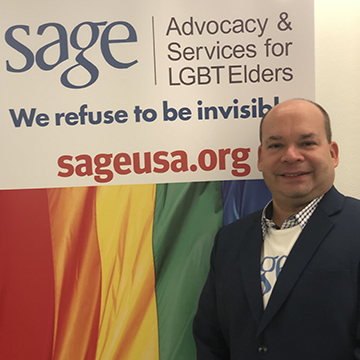 Wilfred Labiosa standing in front of pride flag.