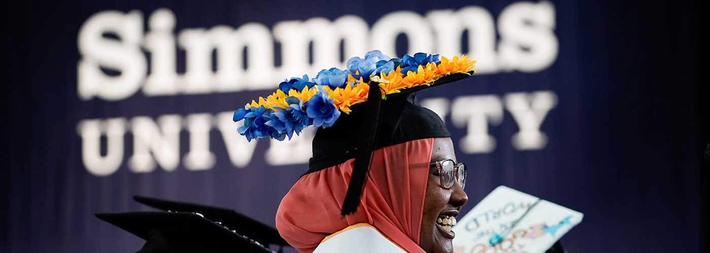 Graduating senior in front of Simmons University banner at Commencement