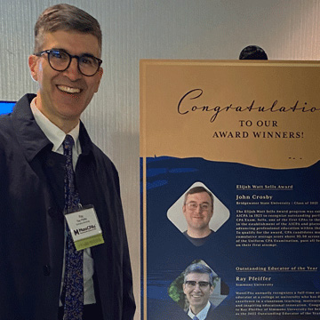 Professor Ray Pfeiffer standing by sign showing his winning MSCPA Award
