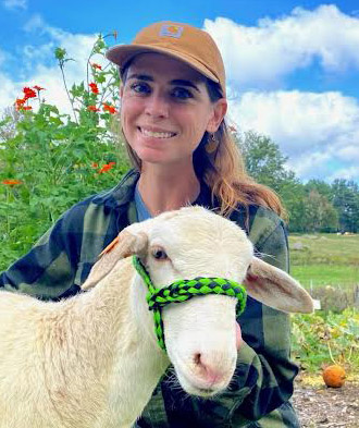 Molly Foye ’23MS facing camera with a sheep also facing camera outdoors at a farm