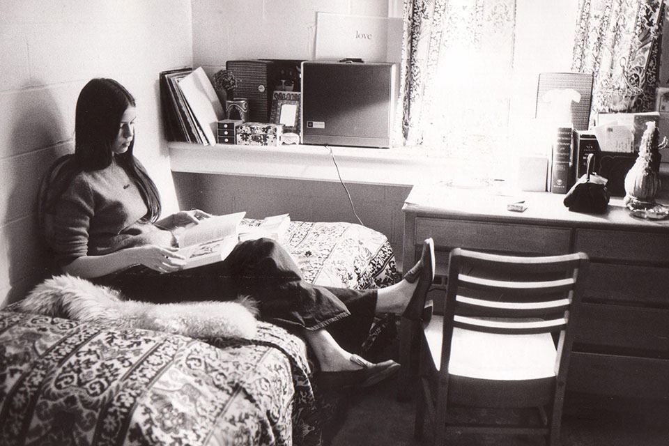 Student sitting on bed studying in dorm room in 1970s
