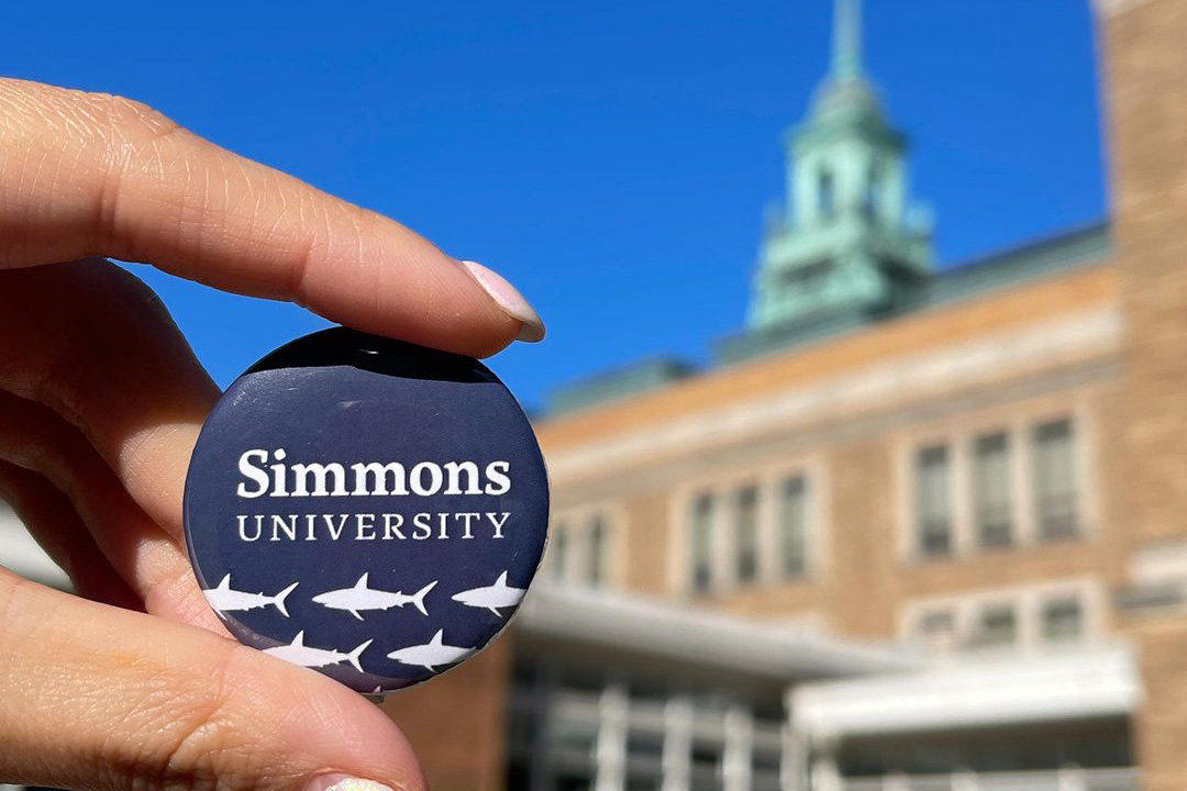 Hand holding a Simmons pin with sharks on it in front of the MCB