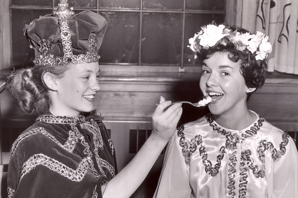 May King Marjorie Burroughs '62 feeds cake to May Queen Grace Richardson '60 at the May Day celebration in 1960, courtesy of Simmons University Archives