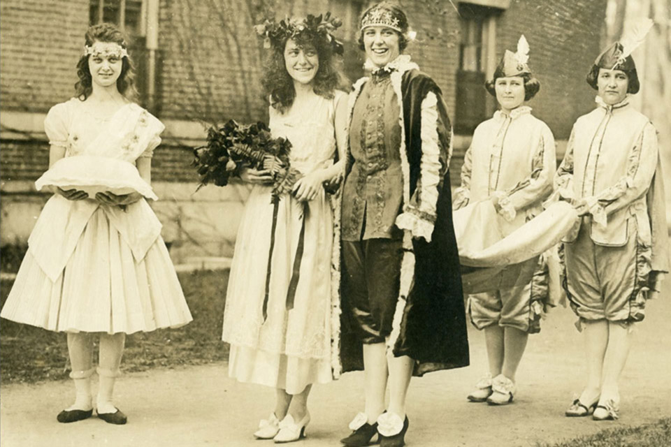 May Queen, May King, and their court processing outside North Hall, 1920.