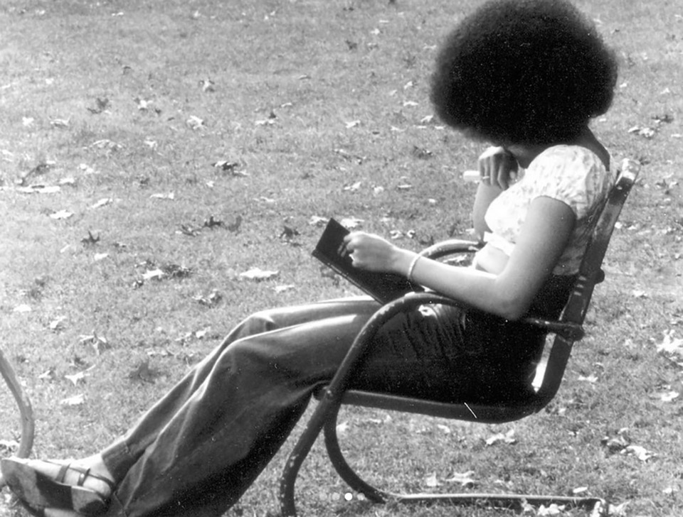 Student reading a book in a chair on the Quad, 1975