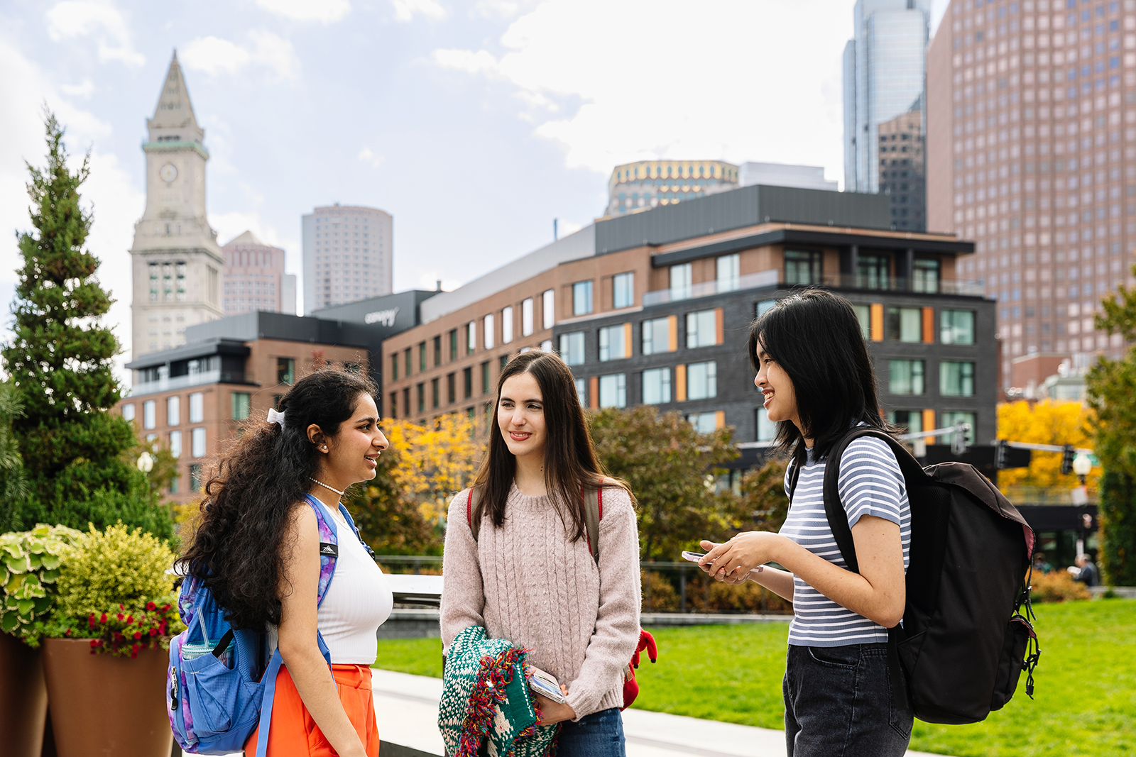 Three Simmons students talking in the Academic quad, with a view of some of Boston's tall buildings in the background