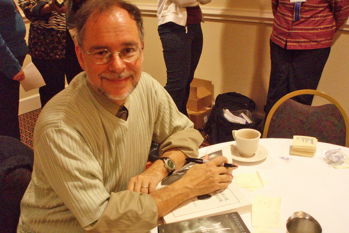 Gregory Maguire seated at a table signing a book