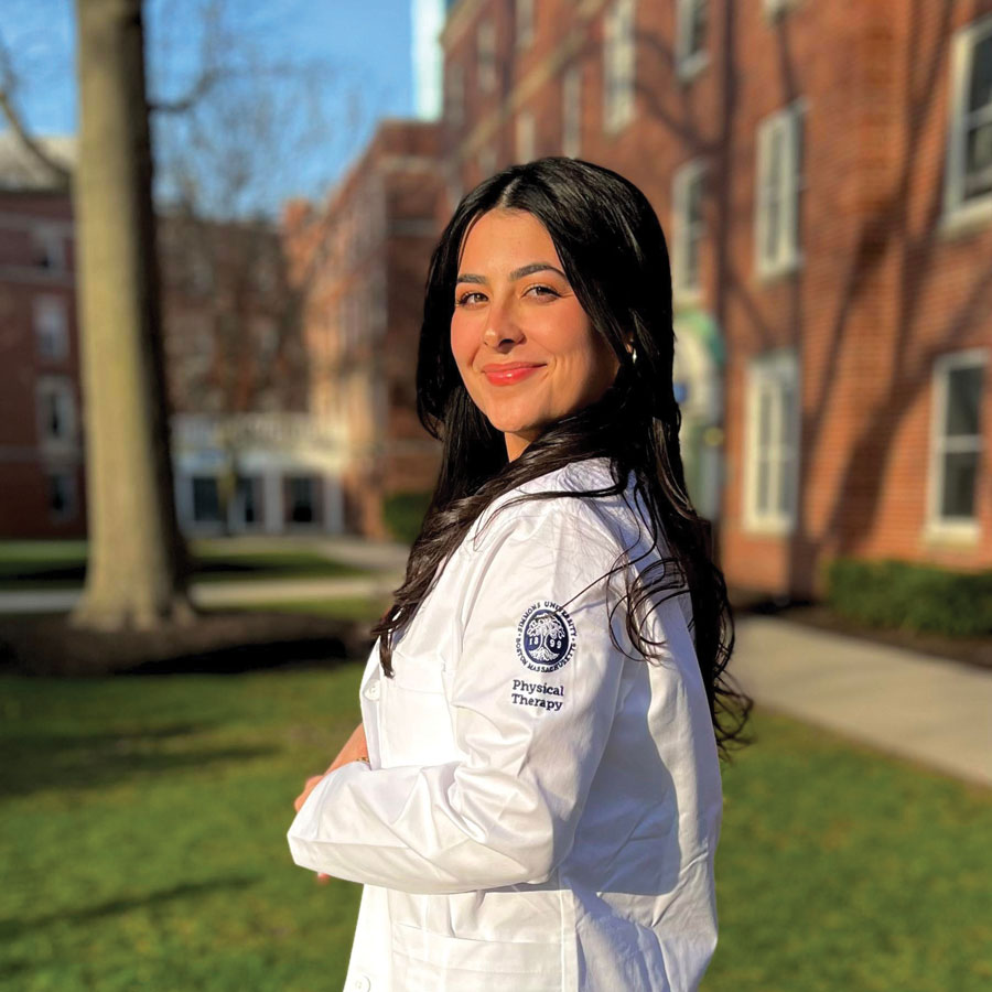 Isabella Carlos ’24DPT wearing a white coat the the Simmons logo and the words Physical Therapy on the shoulder