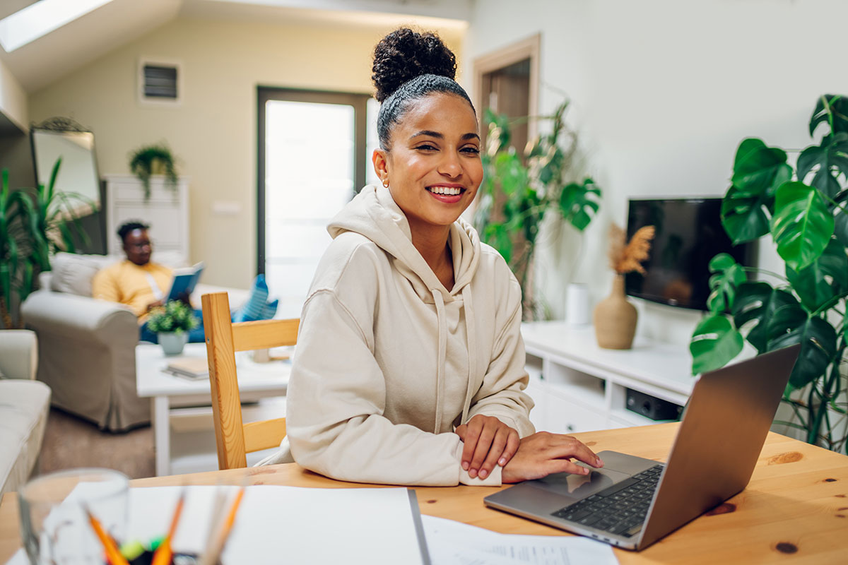 A young woman working ona laptop in her living room surrounded by plants