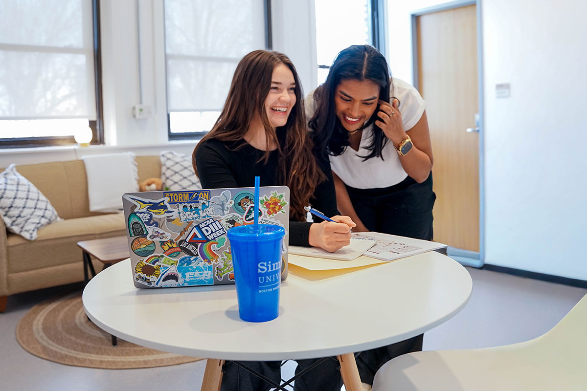 Two Simmons students working together at a round table with a laptop open