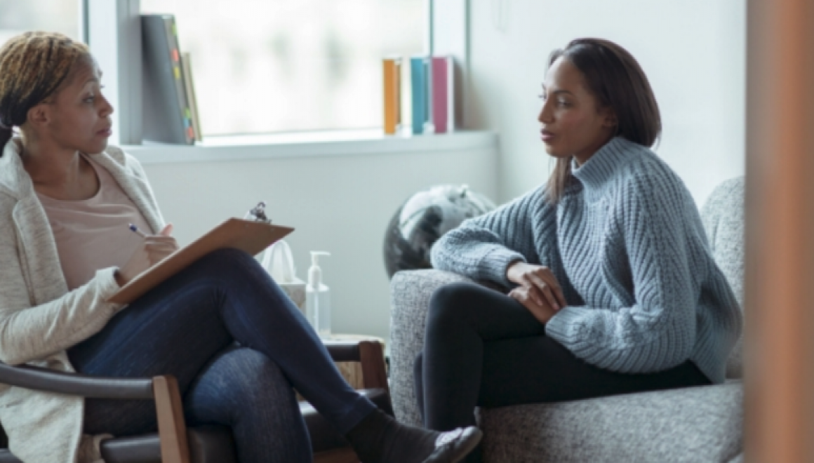 Two women sitting in chairs having a discussion. One woman is holding a clipboard.