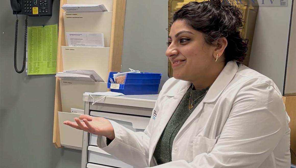 A Simmons Nursing alum wearing a white coat and gesturing as she speaks with a patient 