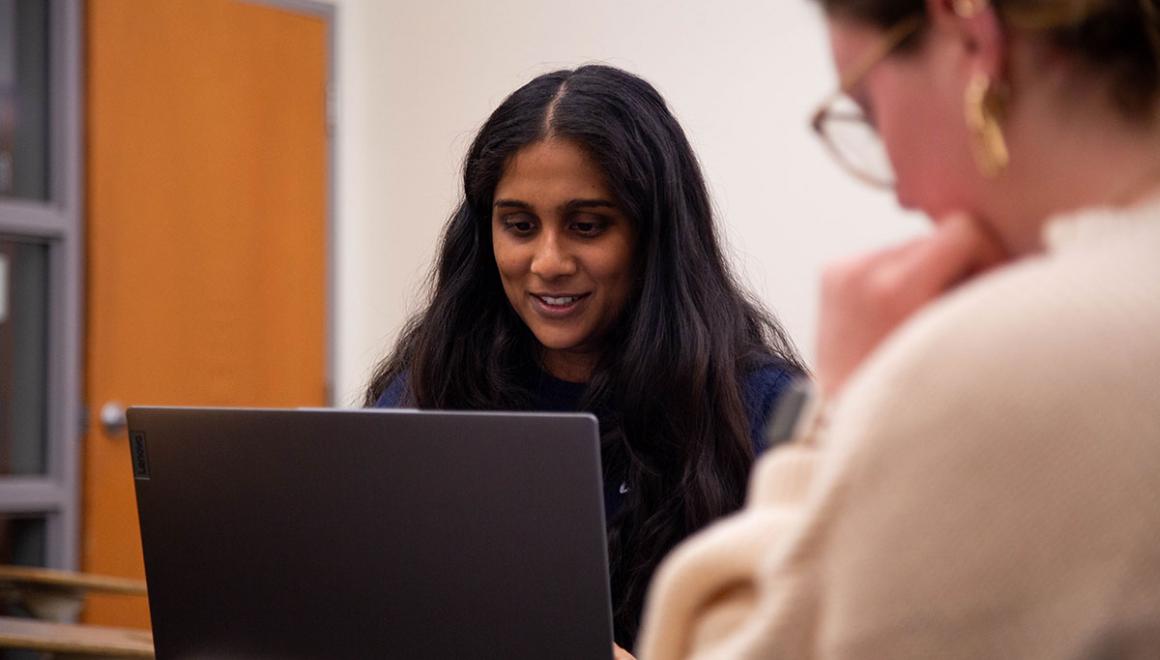 Two Simmons students working together in a class, one has an open laptop