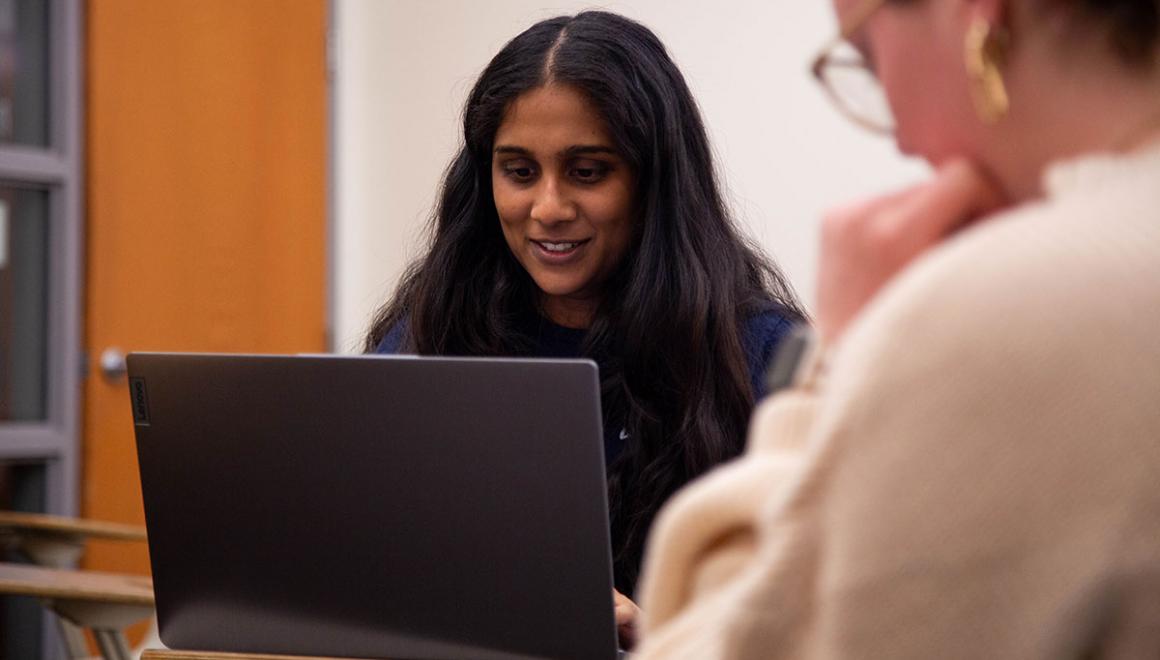 Two Simmons students working together in a class, one has an open laptop