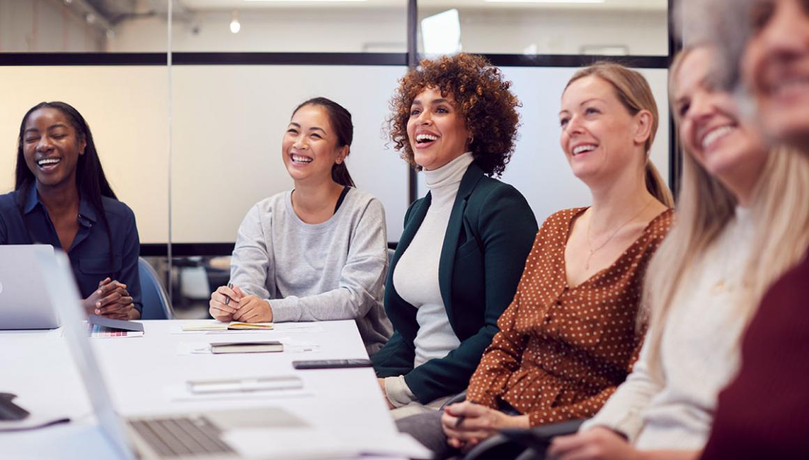 A group of women smiling while seated at a conference table