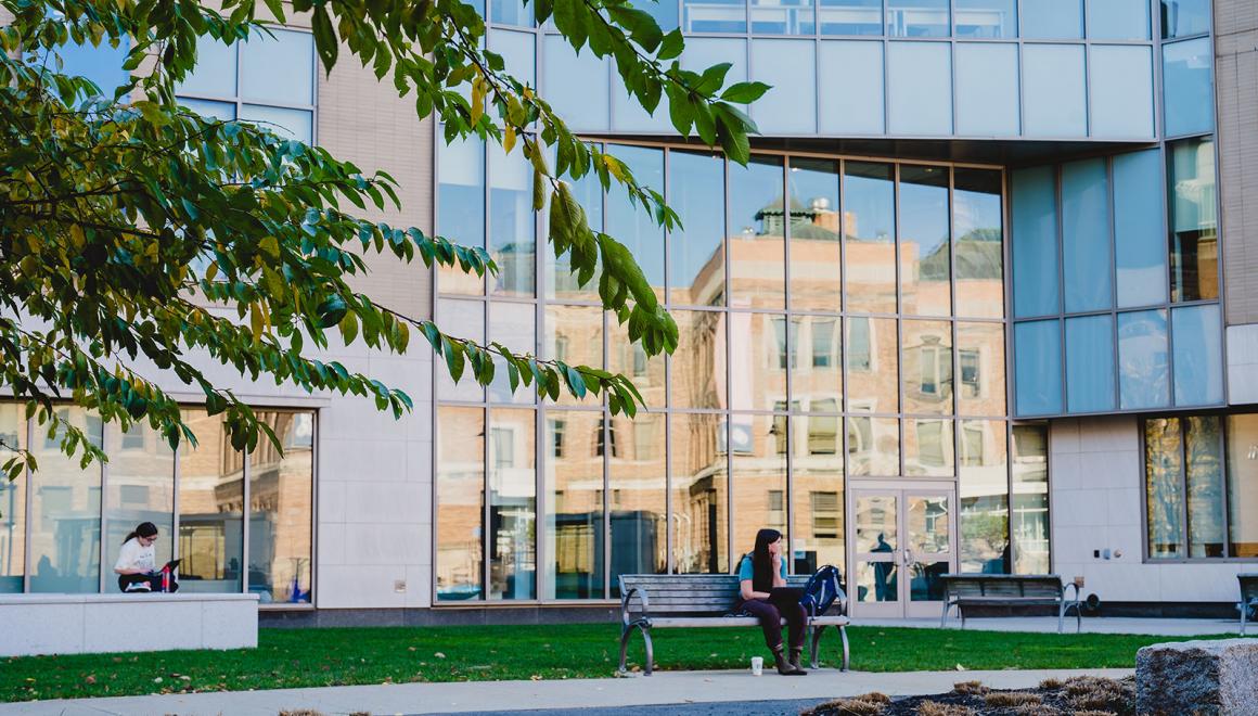A student sits on a bench outside a building on the Simmons University campus