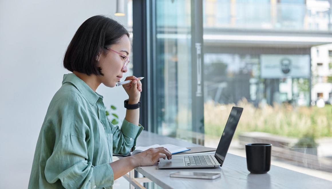 A student working on a laptop at a standing desk by a window