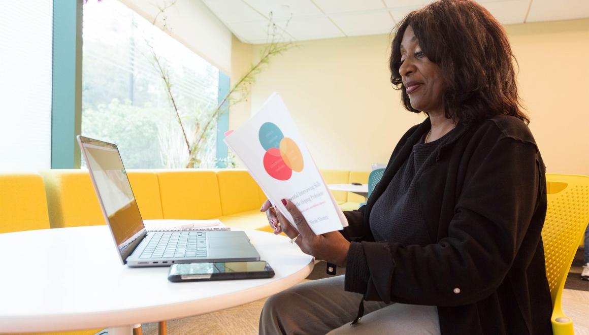 Student reading from book sitting at table with laptop