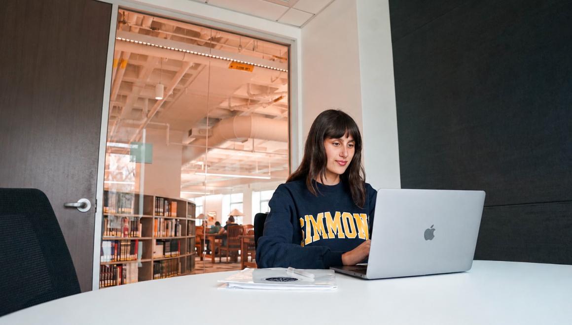 Student in Simmons sweatshirt on laptop in library study room