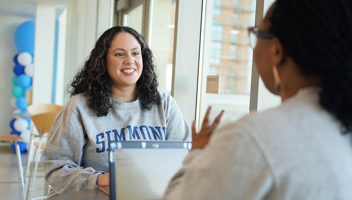 Two MPH students having a conversation while seated near large windows