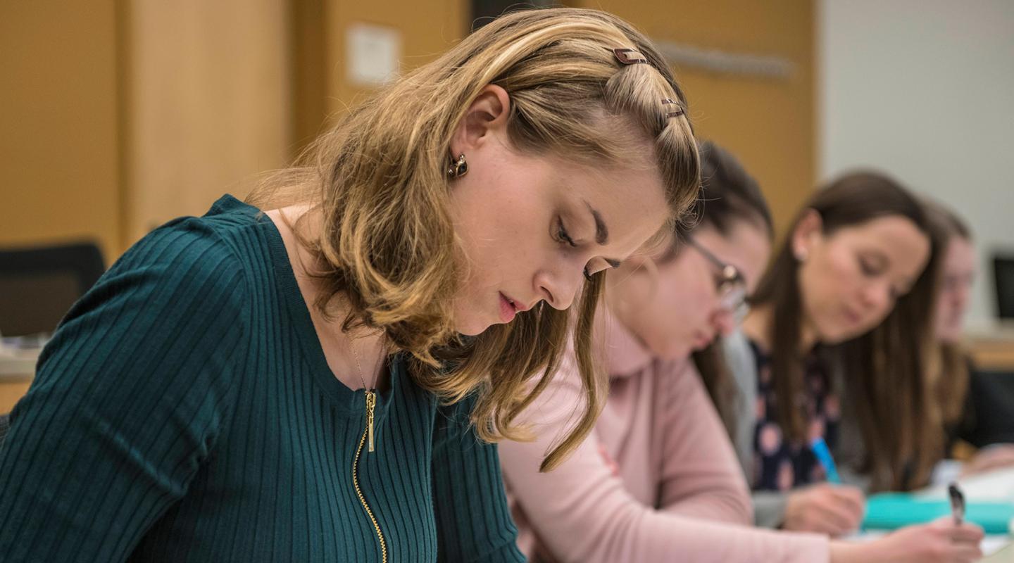 A student sits at a desk in class next to two additional classmates