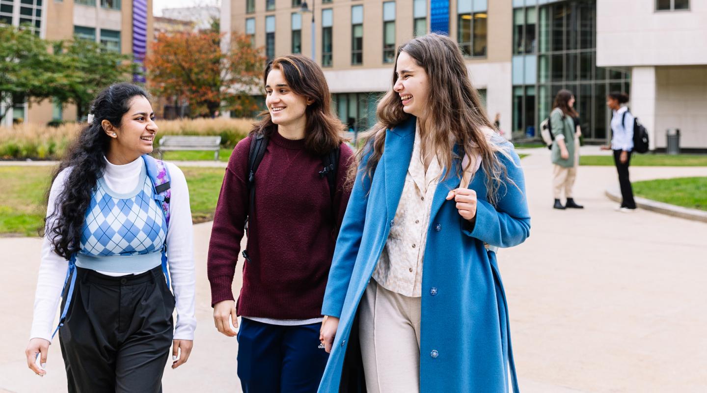 Three smiling Simmons students walking together through the Main Campus Quad
