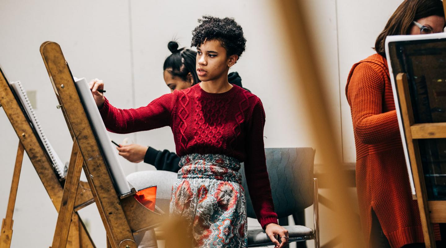 Student standing by easel painting in classroom
