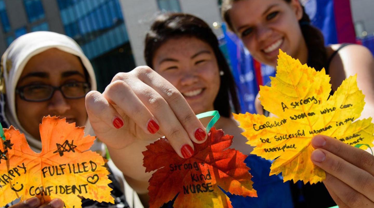 A group of three students holding up colorful fall leaves with their aspirations written on them