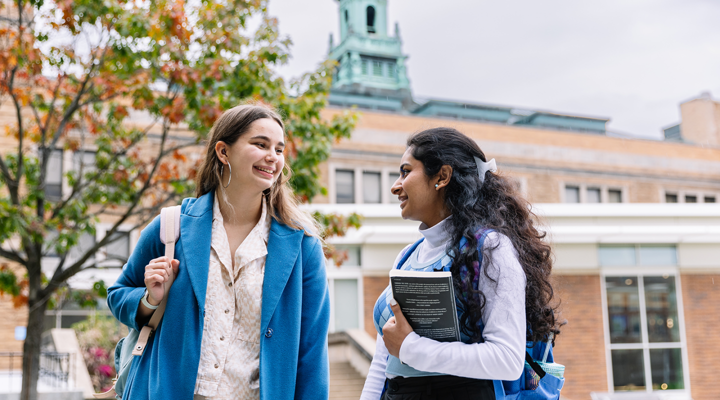 Two Simmons students walking on campus with a view of the iconic cupola in the background