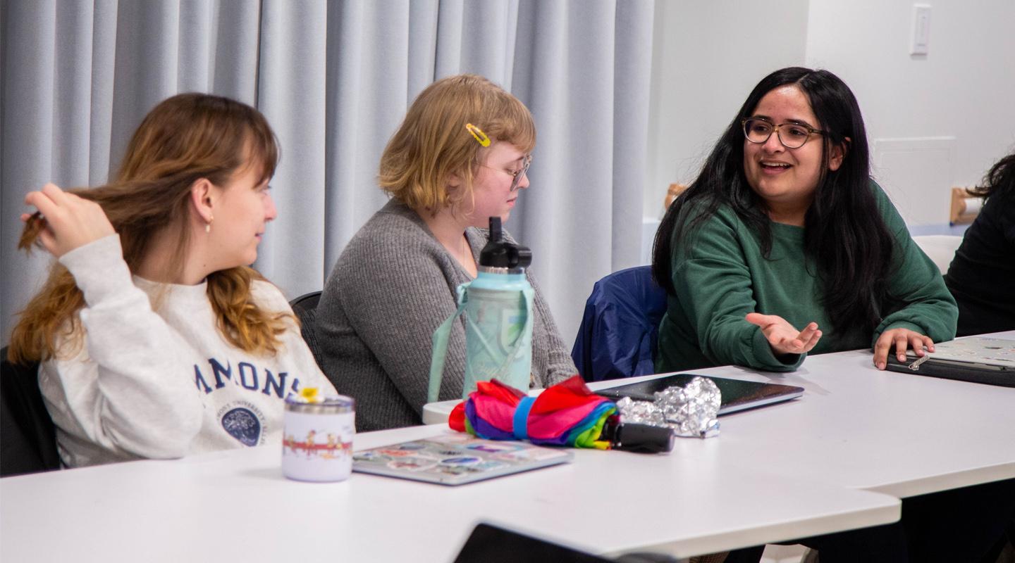 Students talking while sitting at table in feminist media studies class.