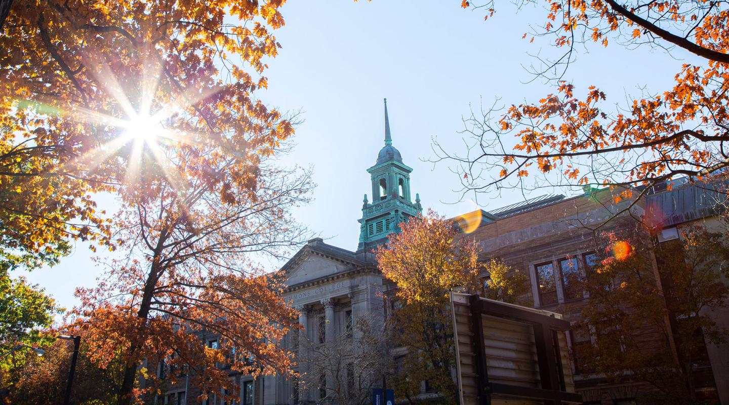 The cupola of the Main College Building on the Simmons University campus, as seen through a tree with colorful fall leaves.