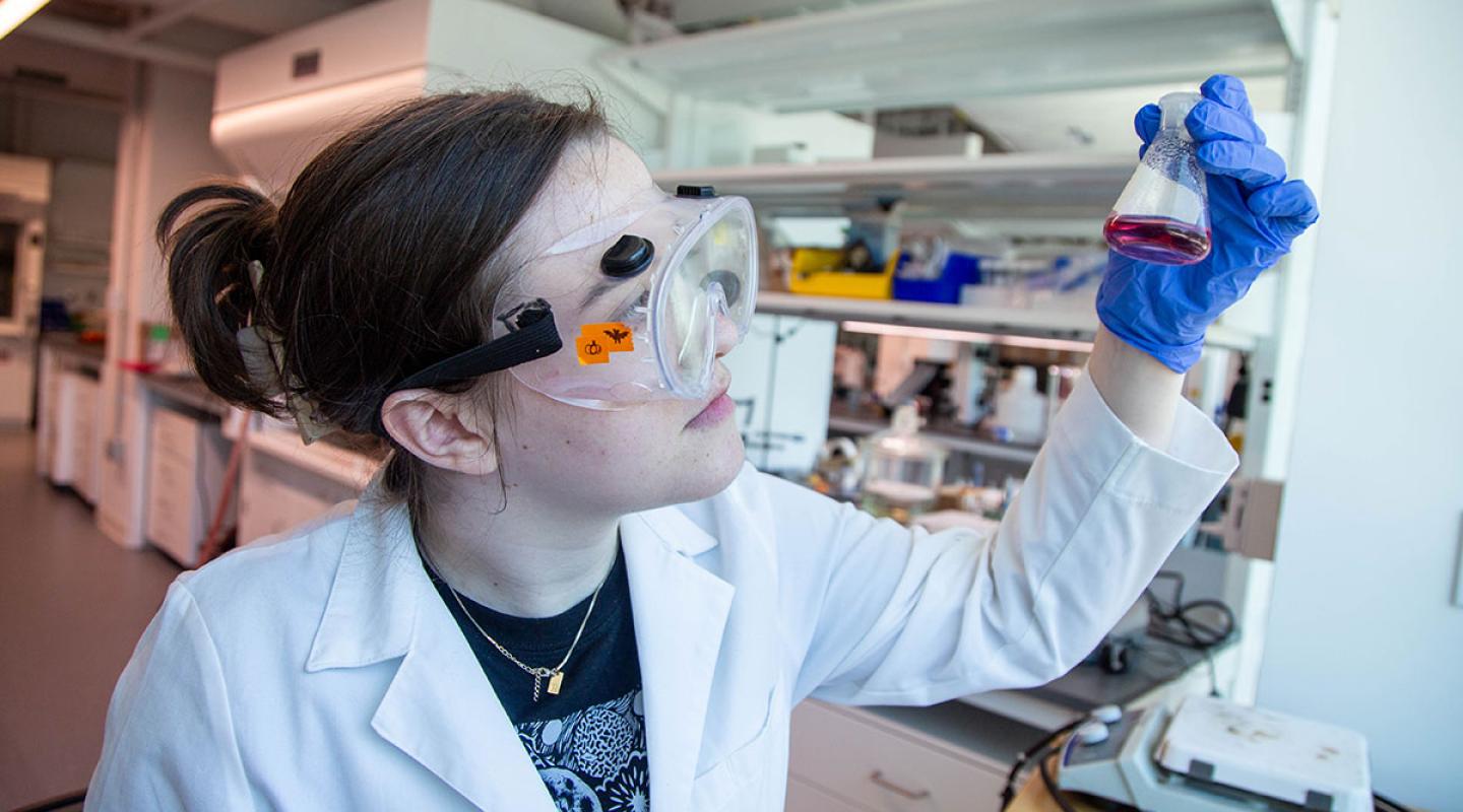 A Simmons student wearing goggles and working in the chemistry lab