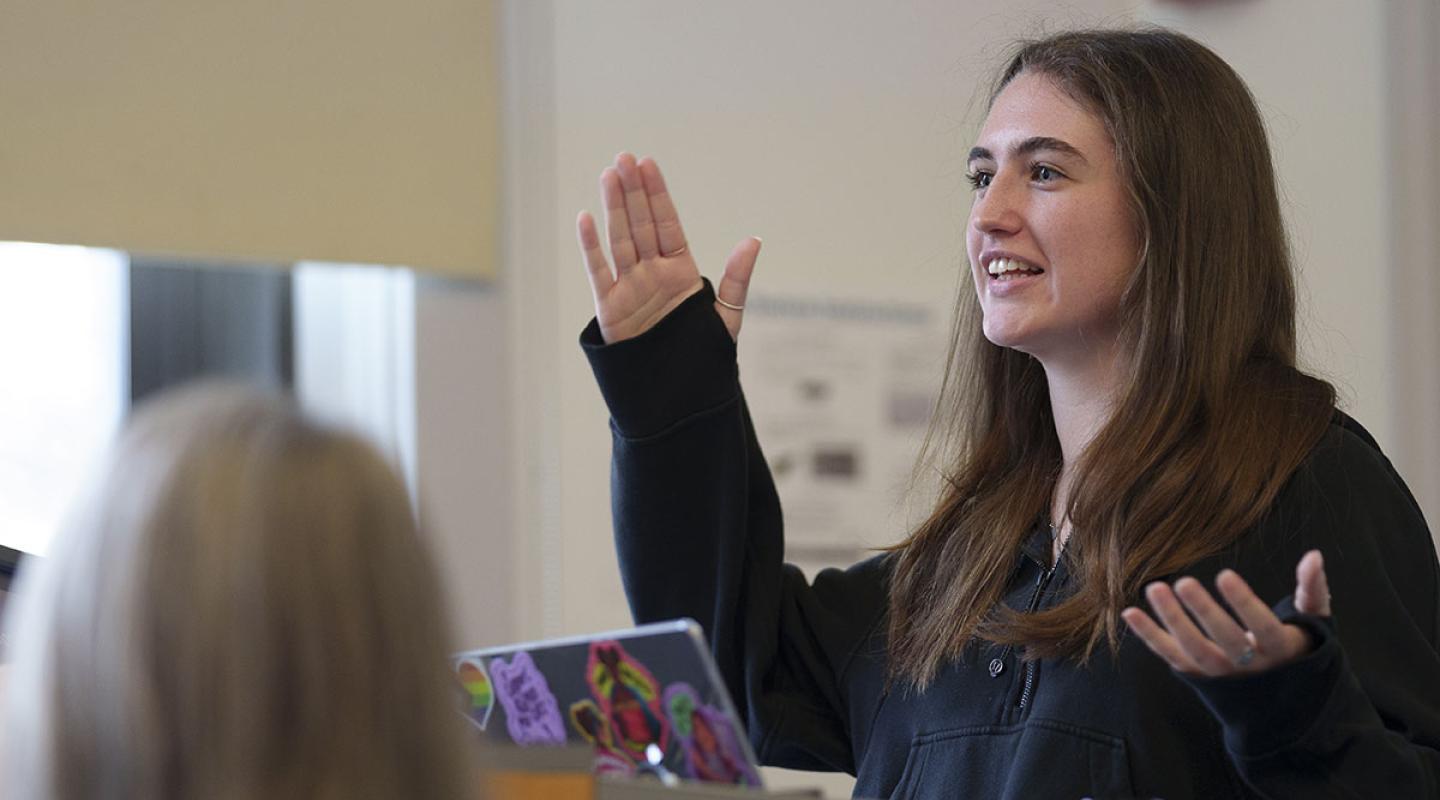 A Simmons student giving a presentation at a podium and gesturing 