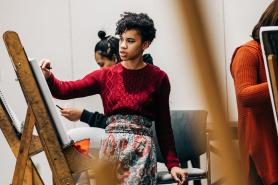 Student standing by easel painting in classroom