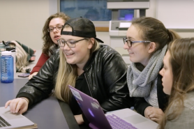 A group of students smiling while looking at a laptop 