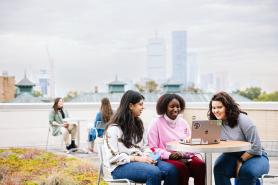 Three Simmons students seated at an outdoor table with the Boston skyline in the background