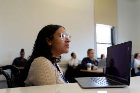 A Simmons student listening attentively during a class. A laptop is open on the desk in front of the student.