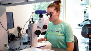 A Simmons University student using a high-powered microscope in the Science Center