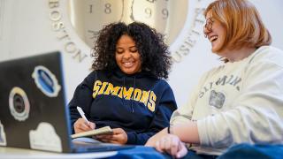 Two Simmons undergraduate students sitting near the University seal in the Main Campus Building