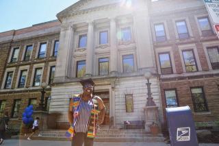 Mardoche Telumsa in front of the Main College Building wearing her graduation regalia