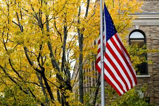 US flag in front of the Simmons University Main College Building in the fall.