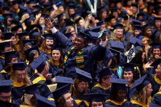 Graduate Student standing cheering amongst fellow graduates