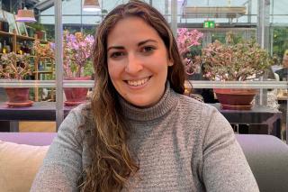 Kaitlin Allair ’21MS sitting on a sofa with many flowering plants behind her