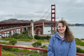 Maddie Gretzky stands on the shore with the Golden Gate Bridge behind her