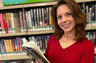 Molly Riportella holding a book amoung shelves of library books