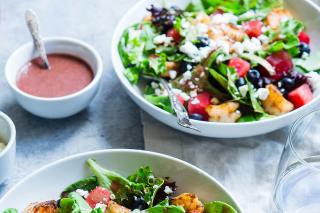 Two bowls of salad with dressing in bowls on the side. 