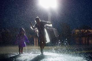 An adult and a child wearing raincoats and dancing in a puddle