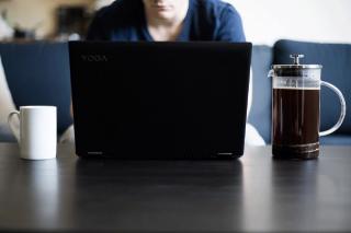 A person seated at a table with an open laptop and cup of coffee