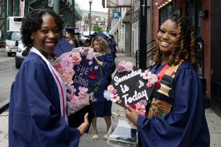 2 graduating students with decorated grad caps.  One cap says "She's Grad," and the other says "Someday is Today"